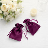 Purple satin drawstring bags on a table with flowers and a candle.