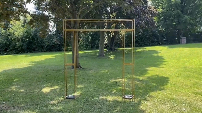 Gold metal 3D rectangular arch placed on a green lawn with trees in the background.