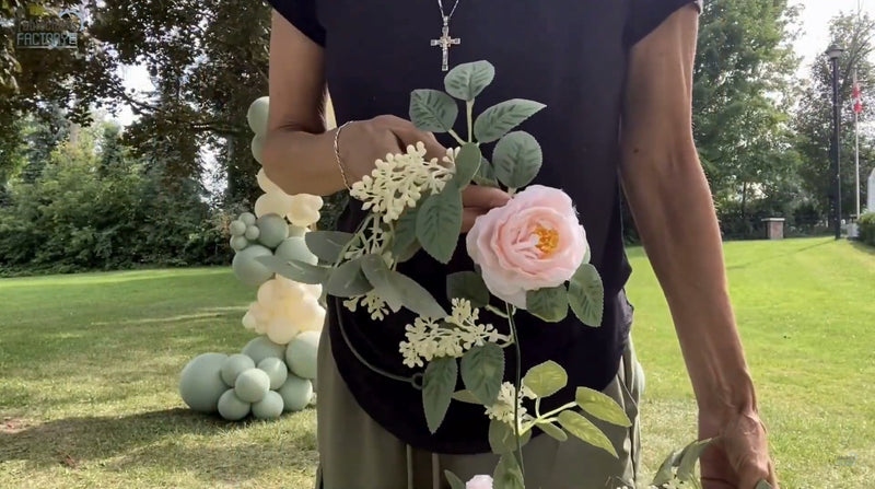 Person holding blush dusty rose artificial flowers with balloon arch in the background.