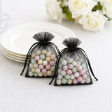 Black organza gift bags with pastel candy balls on a white table.