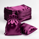 Purple satin drawstring bags and pillows stacked on a white background