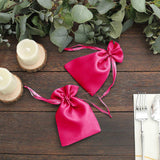 Pink satin gift bags with ribbon ties on a rustic wooden table.