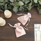 Pink satin drawstring bags on a wooden table with greenery and candles.