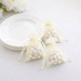 Pastel candy favors in organza bags with white plates on a soft table setting