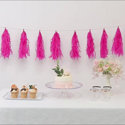 Pink tissue paper tassel garland for party décor with cupcakes and cake.