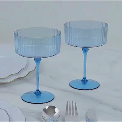 Dusty blue disposable coupe champagne glasses on a marble surface.