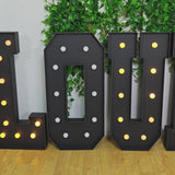 Black LED marquee letter "P" with warm white lights on a leafy background.