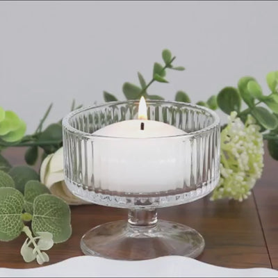 Two lit candles in glass holders with warm fairy lights on marble surface