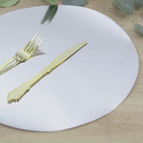 Silver round disposable table placemat with gold cutlery on a wooden surface.