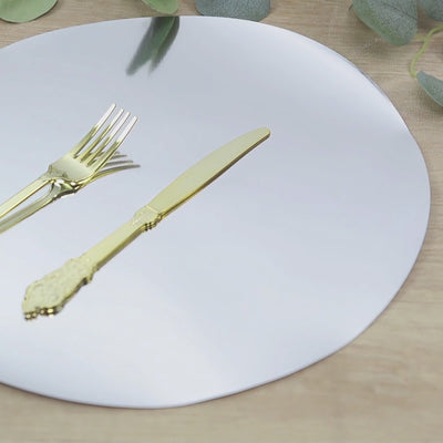 Silver round disposable table placemat with gold cutlery on a wooden surface.