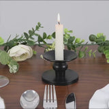 Black metal candle holder with a white candle, elegant table setting.