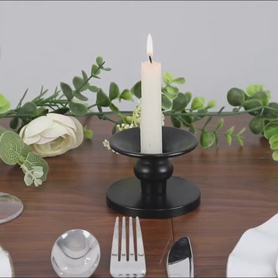 Black metal candle holder with a white candle, elegant table setting.