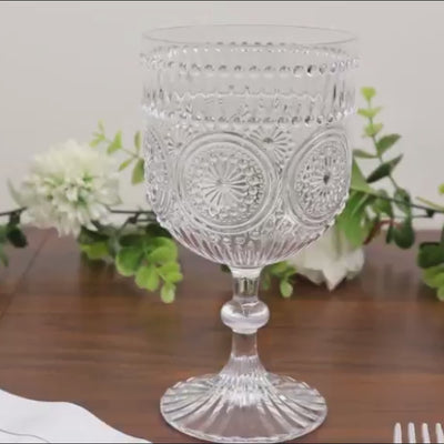Clear vintage plastic wine goblets with embossed floral pattern on a wooden table.