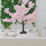 Blush pink artificial cherry blossom tree centerpiece on a dining table.