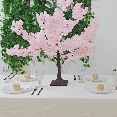 Blush pink artificial cherry blossom tree centerpiece on a dining table.
