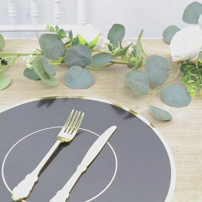 Black round disposable placemat with gold rim on a table setting.
