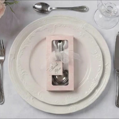 Engraved silver heart measuring spoons in a gift box on a white plate.