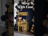 Gold dessert cart with floral arrangement against a festive balloon backdrop.