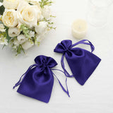 Purple satin drawstring bags next to white flowers and a candle.