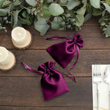 Purple satin drawstring bags on a rustic wooden table with greenery and candles.