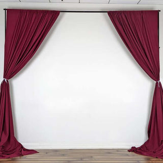 Burgundy fabric drapes hanging elegantly against a plain backdrop.