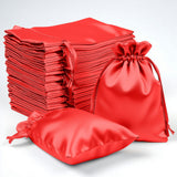 Red satin drawstring bags stacked and displayed on a plain backdrop.
