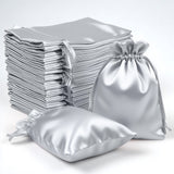 Silver satin drawstring bags stacked and arranged on a white backdrop.