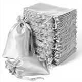 Stack of elegant silver satin drawstring bags on a white background