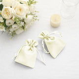 Two elegant satin favor bags in pale yellow beside a bouquet of white roses.