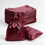 Burgundy satin drawstring bags stacked and one bag open on a white background
