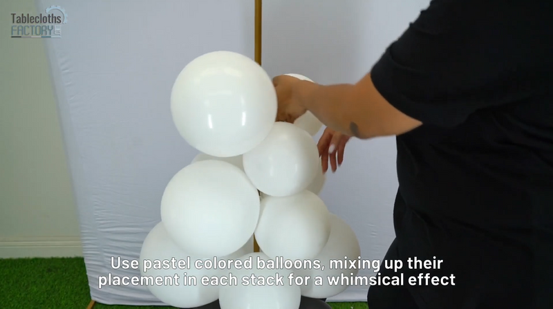 Person arranging white balloons on a balloon column stand, creating a whimsical stack against a white spandex backdrop.