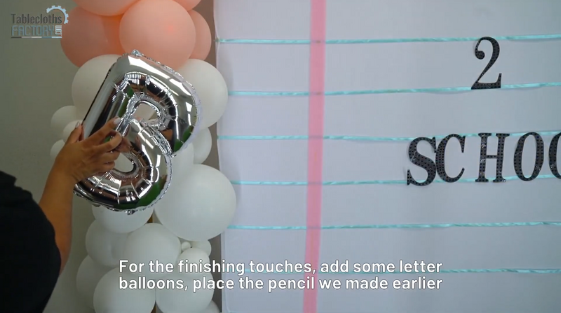Person placing a silver letter balloon on a colorful balloon column next to a 'back to school' themed backdrop.