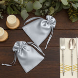 Silver satin drawstring bags on a rustic wooden table with candles and cutlery.