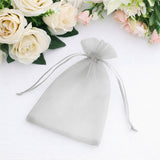 Silver organza gift bag with drawstring closure on a floral background.