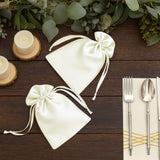 Elegant ivory satin favor bags with drawstring ties on a rustic wooden table.