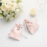Two pink satin drawstring bags beside white flowers and a candle.
