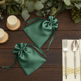 Green satin drawstring bags on a wooden table with candles and cutlery.