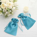 Turquoise satin gift bags with tied ribbons, styled with flowers and a candle.