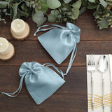 Blue satin drawstring bags on a wooden table with candles and cutlery.