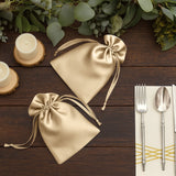 Gold satin drawstring bags on a wooden table with candles and cutlery.