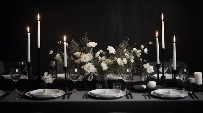 A sleek, minimalist table with black linens, white dishes, and tall black candles.