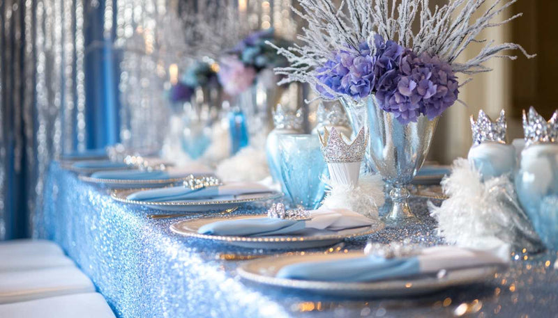 A fairytale-inspired baby shower with icy blue, silver, and purple accents, princess crown napkin holders, and shimmering decor like snowflakes and icicles. Perfect for a magical winter wonderland celebration.