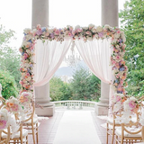 Floral wedding arch with draped fabric and chairs in an outdoor venue.