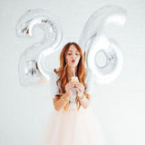 Woman celebrating 26th birthday with cupcake and silver balloons.