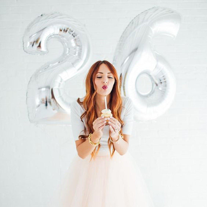 Woman celebrating 26th birthday with cupcake and silver balloons.