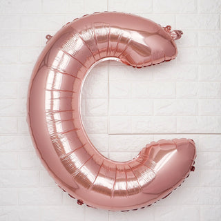 Rose gold foil letter "C" balloon against a white background.