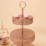 Rose gold two-tier cake stand with decorative patterns and pink macarons.