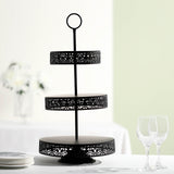 Black three-tier serving stand with ornate design on a table.