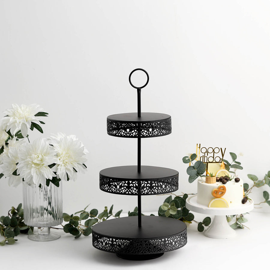 Black three-tiered serving stand with decorative edges on a plain backdrop.
