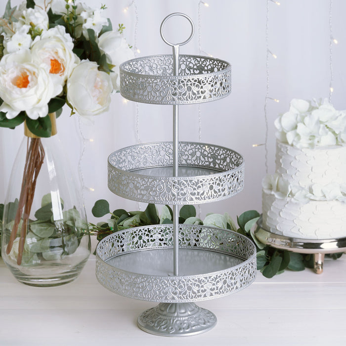 Three-tiered silver serving tray with decorative cutouts in a styled setting.